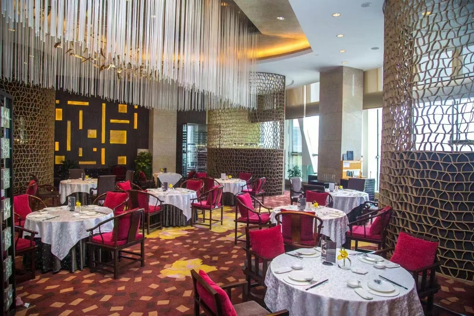 Un restaurante con mesas redondas, sillas rojas y un suelo estampado.