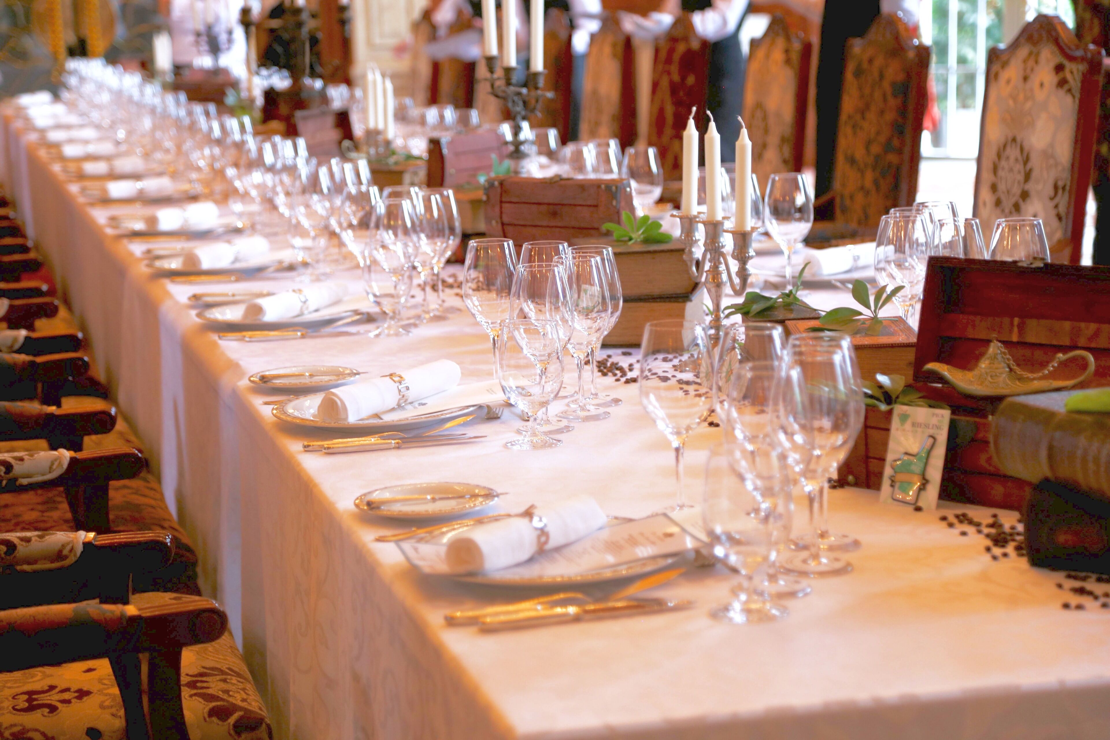 A long dining table set with multiple wine glasses, plates, and cutlery, surrounded by ornate chairs.