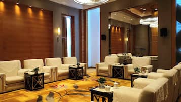 A hotel lobby with a seating area, a large mirror, and a floral carpet.