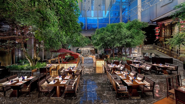 A spacious indoor dining area with multiple tables and chairs, a central walkway, and a large tree providing shade. - InterContinental Chengdu Century City by IHG (Chengdu)