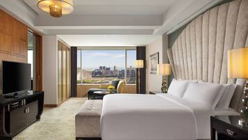 A hotel room with a large bed, a TV, a desk, and a view of the city.