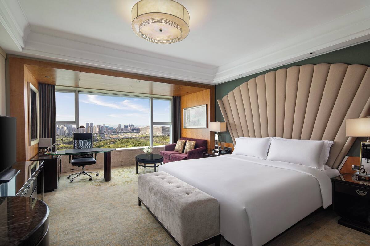 A hotel room with a large bed, a desk, a chair, and a view of the city.
