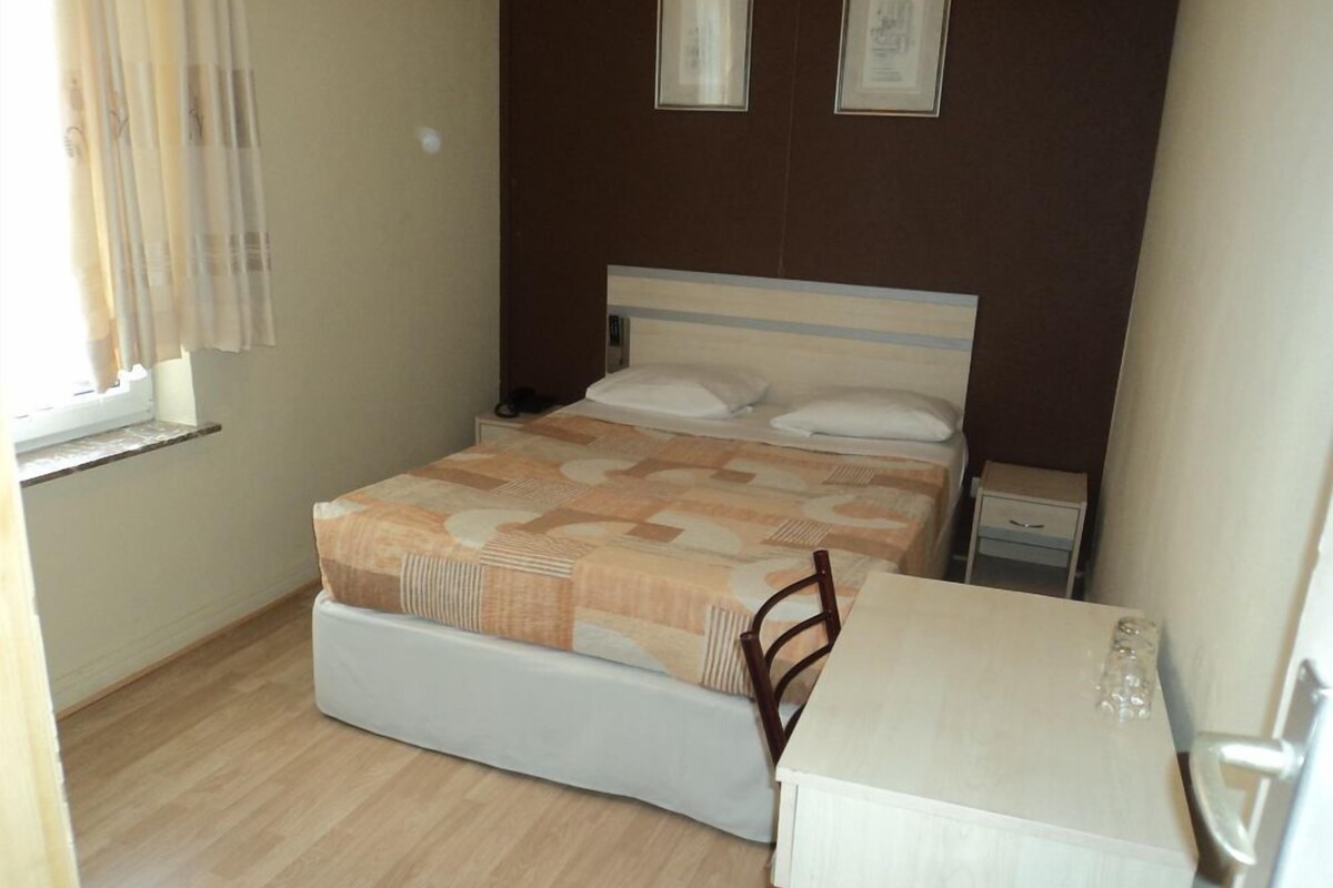 Une chambre à coucher avec un lit, une table de chevet, une chaise et une fenêtre avec des rideaux.