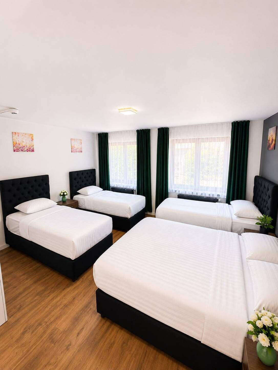 A hotel room with three beds, a wooden floor, and green curtains.