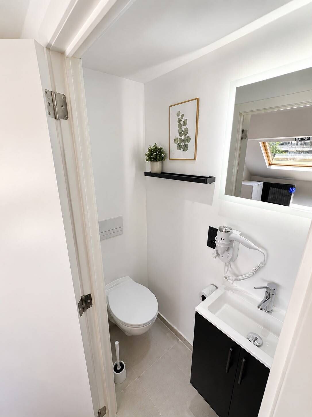 Une petite salle de bain comprenant des toilettes, un lavabo et une petite étagère sur laquelle est posée une plante.