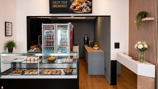 Un área de desayuno con una vitrina de pasteles, un refrigerador y un cartel en la pared.
