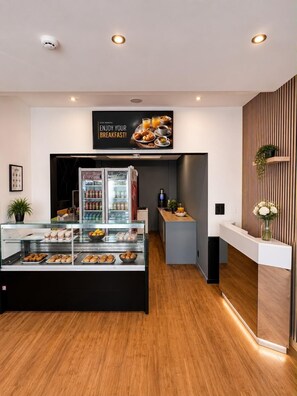 A breakfast area with a display case of pastries, a refrigerator, and a wall-mounted sign. - Hotel Albergo (Brussels)