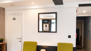 A room with two green armchairs, a small wooden table with a lamp and a potted plant, a framed picture on the wall, and a door labeled 'WC DAMES'. - Hotel Albergo (Brussels)