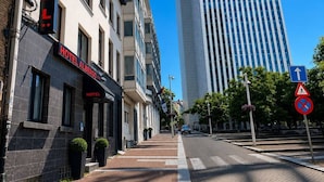 A hotel with a modern facade, a clear sky, and a tall building in the background. - Hotel Albergo (Brussels)