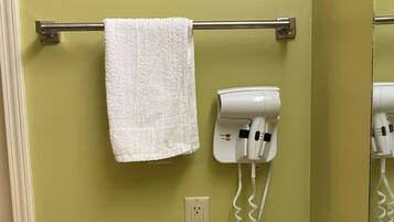 A bathroom with a towel hanging on a metal rod, a hairdryer mounted on the wall, and an electrical outlet below.