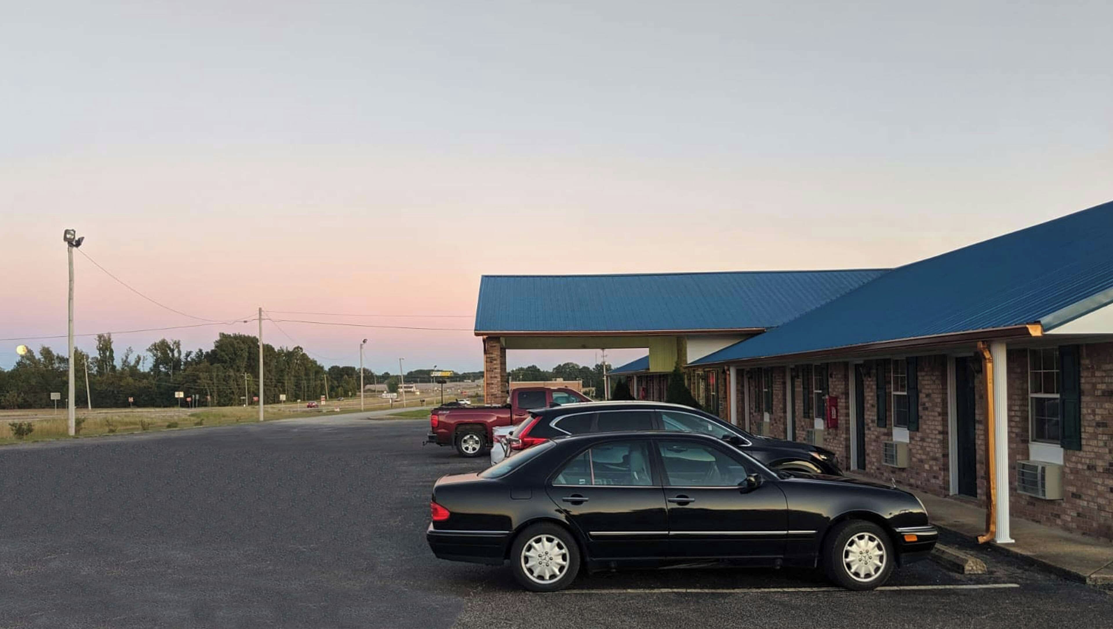 A building with a blue roof, a parking lot, and two parked cars.