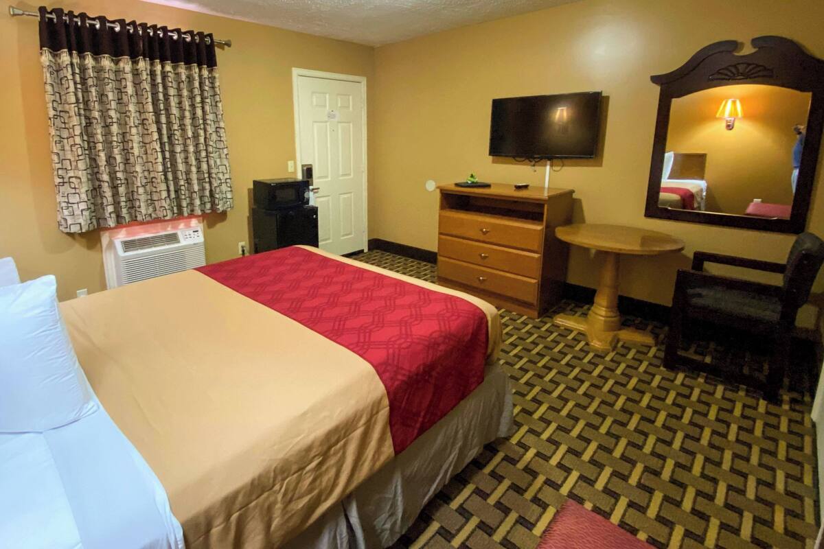 A hotel room with a bed, a desk, a chair, a television, a mirror, and a patterned floor.