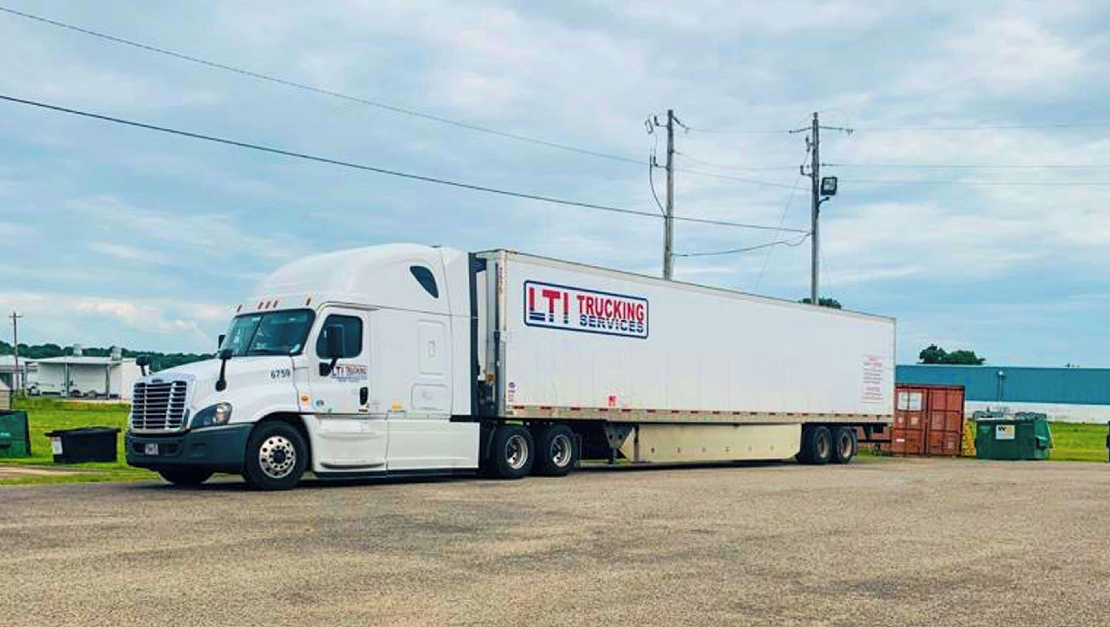 En vit lastbil med släp, med texten ”LTI Trucking Services” på sidan, stod parkerad på en grusplan.