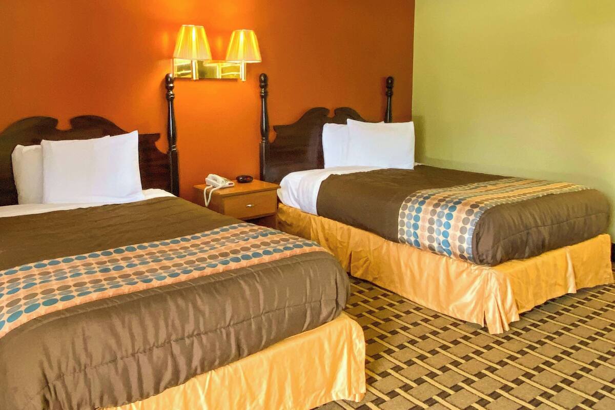 A hotel room with two beds, a nightstand with a phone, and wall-mounted lamps.