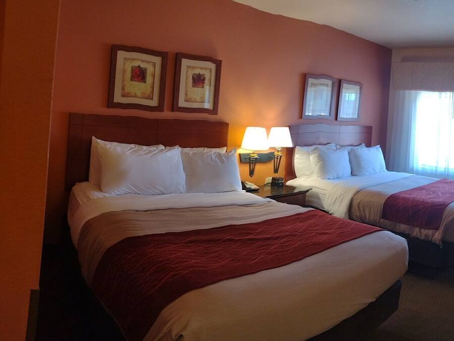 Una habitación de hotel con una cama grande, una cama más pequeña, una silla, una mesa y un televisor.