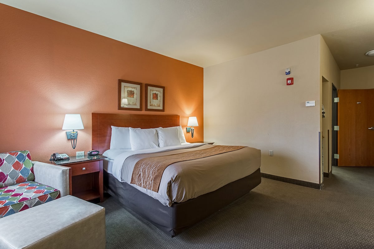 Une chambre d’hôtel comprenant un lit, des tables de chevet, une chaise et une lampe fixée au mur.