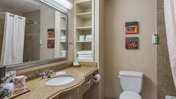 A bathroom with a granite countertop sink, a mirror, a toilet, and a towel rack.
