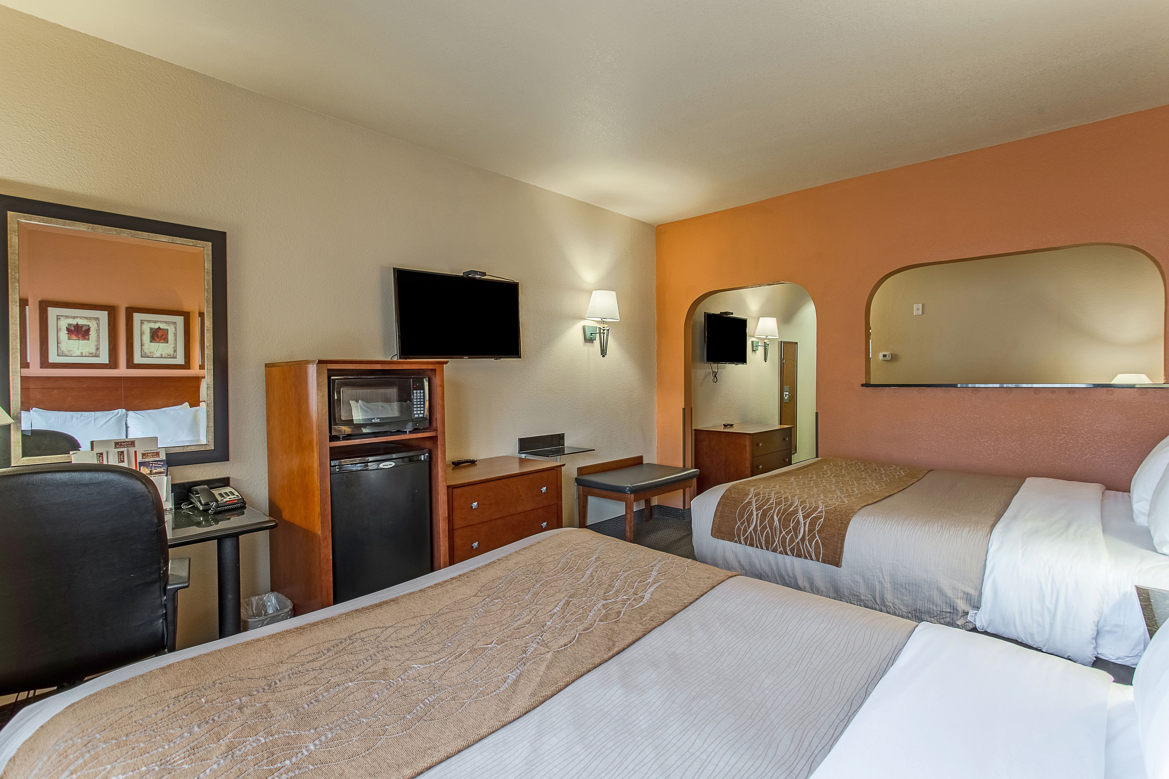 A hotel room with two beds, a desk with a computer, a television, and a microwave.