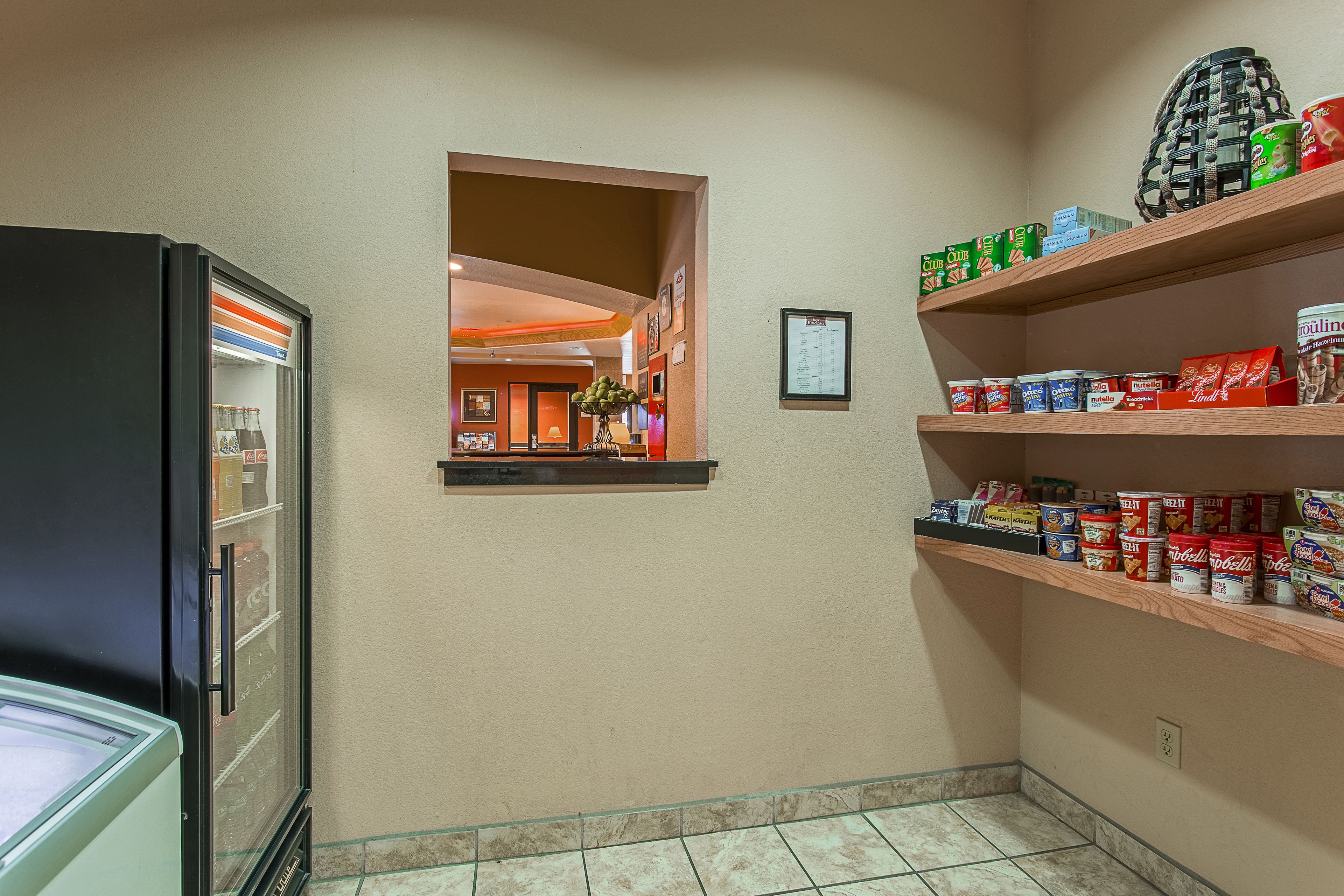 A hotel corridor with a refrigerator, a small window, and shelves with food items.