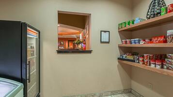 A hotel corridor with a refrigerator, a small window, and shelves with food items.