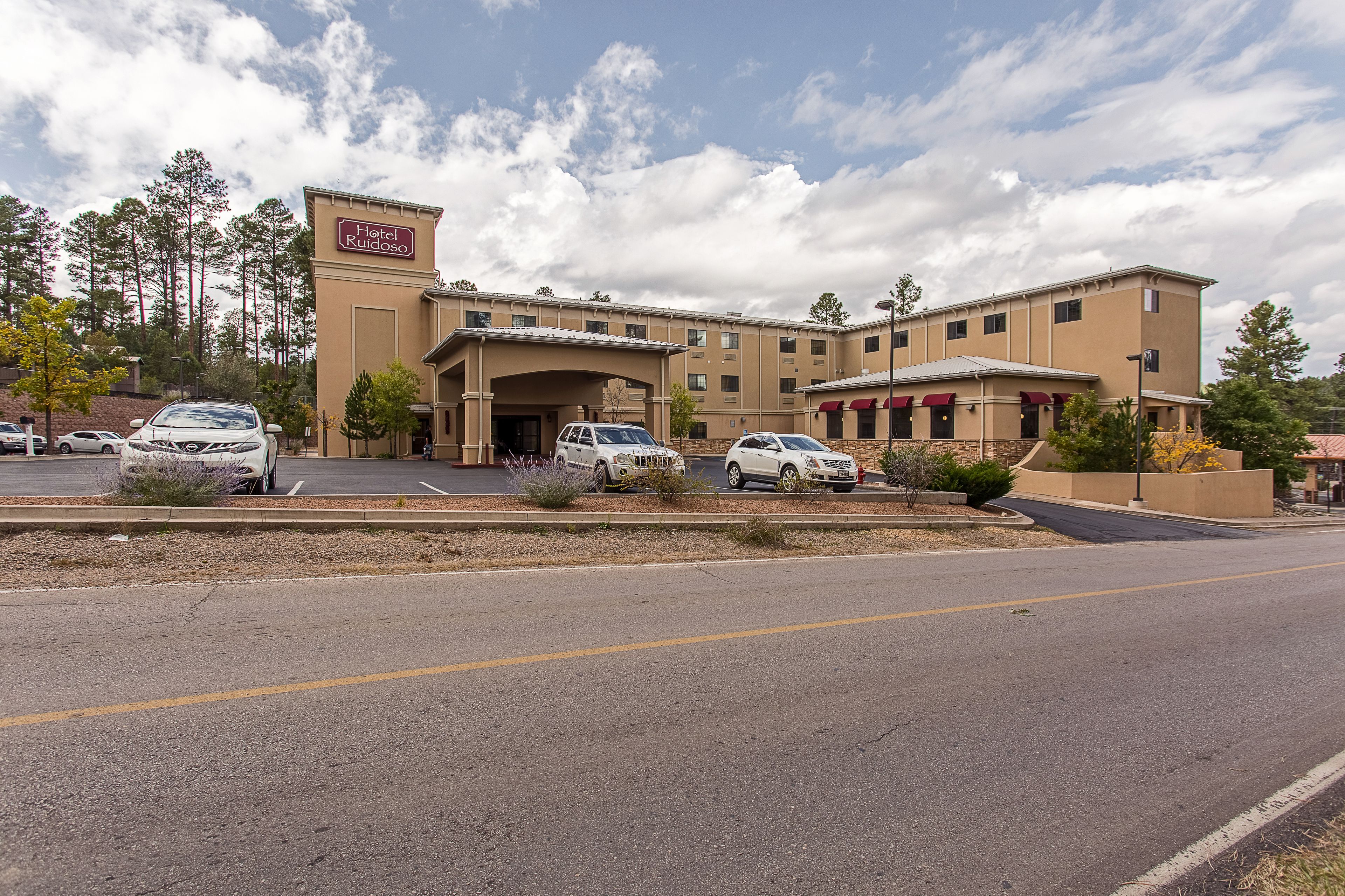 A hotel with a parking lot, multiple cars, and a clear sky.