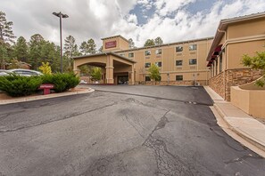 A hotel entrance with a clear driveway, a sign indicating the entrance, and a building with a beige facade and multiple windows. - Hotel Ruidoso - Midtown (Ruidoso)