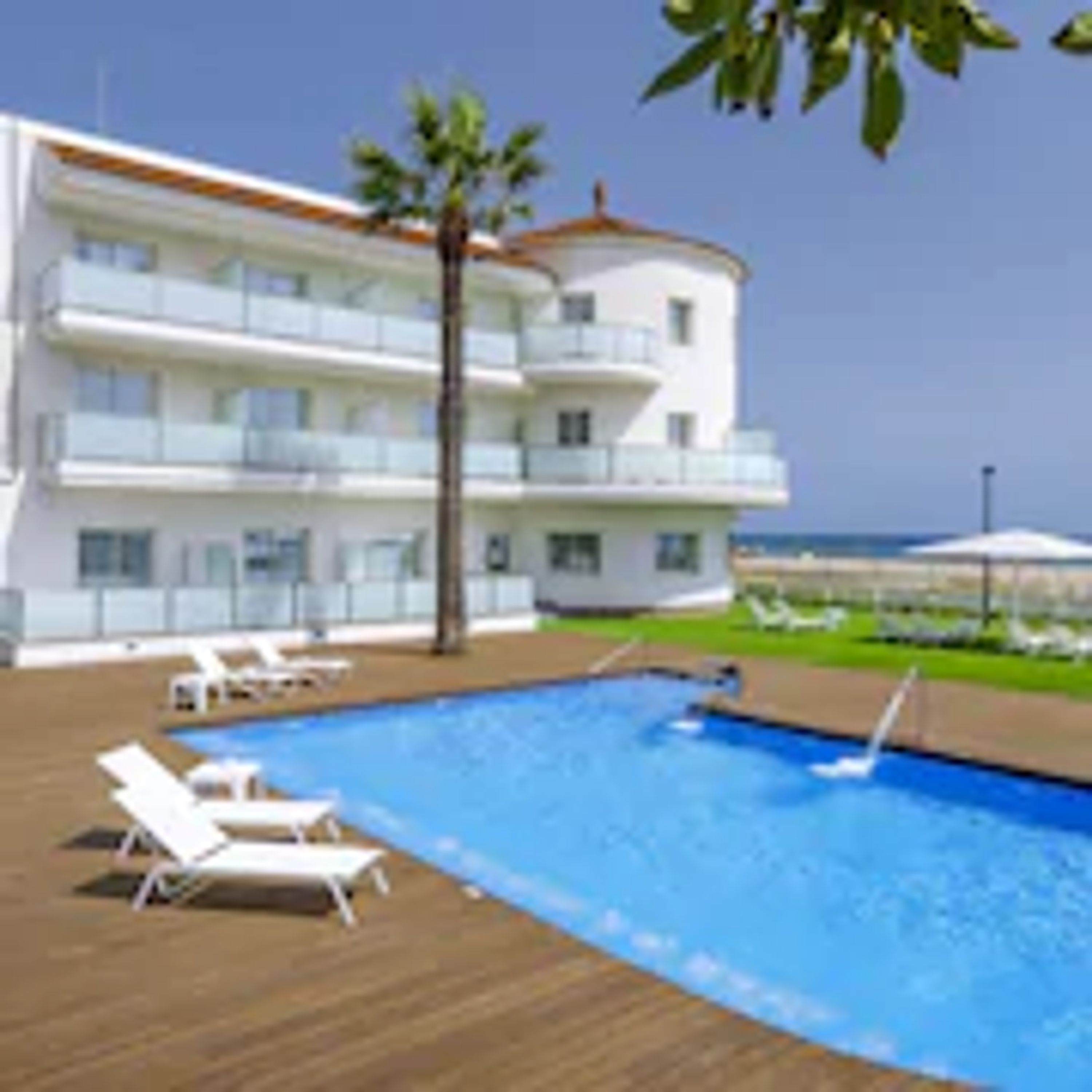 A hotel with a swimming pool, multiple balconies, and a view of the sea.