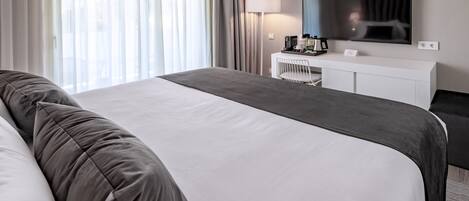 A modern hotel room with a large bed, a bedside table, a flat-screen TV, and a desk with a lamp.
