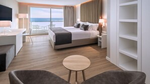 Ein modernes Hotelzimmer mit einem großen Bett, einem Schreibtisch, zwei Sesseln und einem Balkon mit Meerblick.