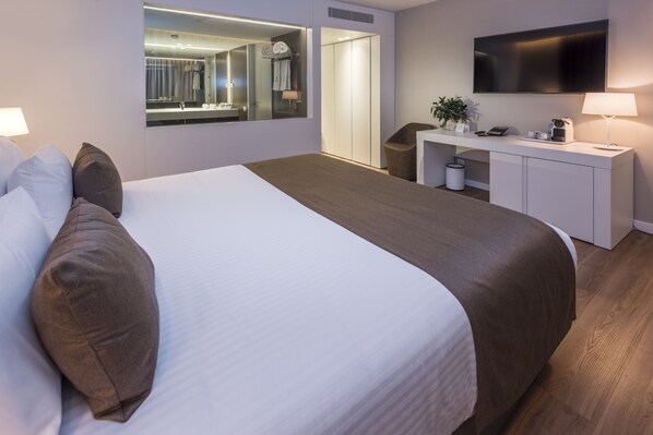 A modern hotel room with a large bed, a desk with a flat-screen TV, a mirror, and a small plant. - Hotel Playafels (Castelldefels)
