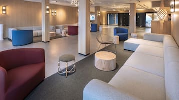 Een moderne hotellobby met een ruim zithoek, een receptiebalie en een groot raam.