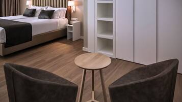A modern hotel room with a bed, bedside tables, a round wooden table, and two armchairs.