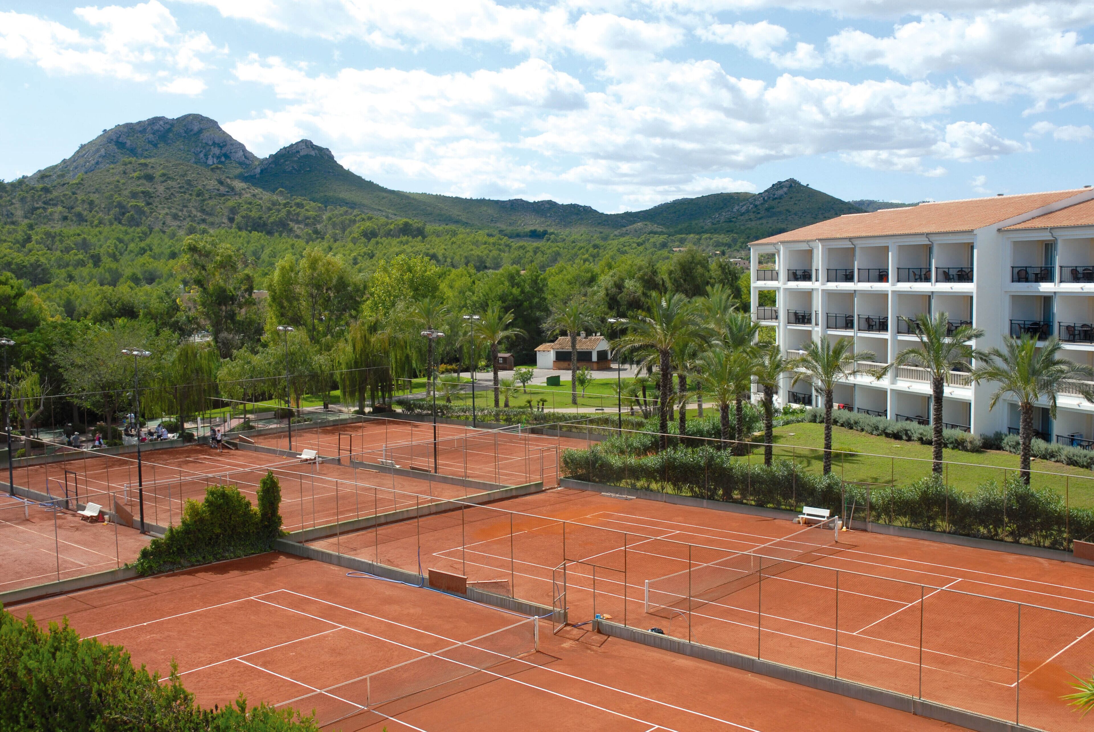 A tennis court with a view of a hotel and mountains in the background.