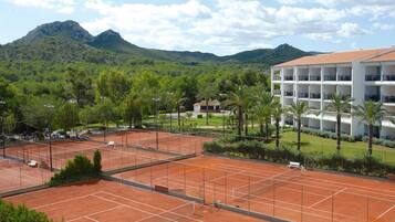 A tennis court with a view of a hotel and mountains in the background.