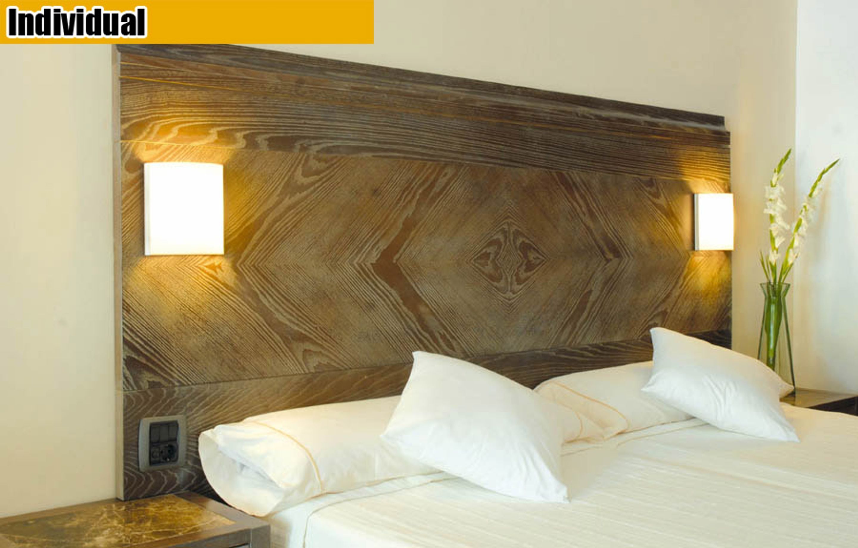 Ein Hotelzimmer mit einem hölzernen Kopfteil, zwei Nachttischlampen, einem Bett mit weißer Bettwäsche und einem Nachttisch mit einem Blumenstrauß.