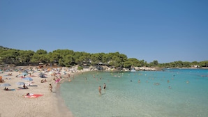 A beach with clear turquoise water, people swimming and sunbathing, and a forested hillside in the background. - FERGUS Club Font de Sa Cala Beach (Capdepera)