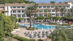 A hotel with multiple floors, a central pool area with lounge chairs and umbrellas, and palm trees. - FERGUS Club Font de Sa Cala Beach (Capdepera)