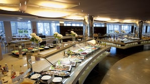 A buffet with various food stations, a seating area with tables, and a large window providing a view of the outdoors. - FERGUS Club Font de Sa Cala Beach (Capdepera)