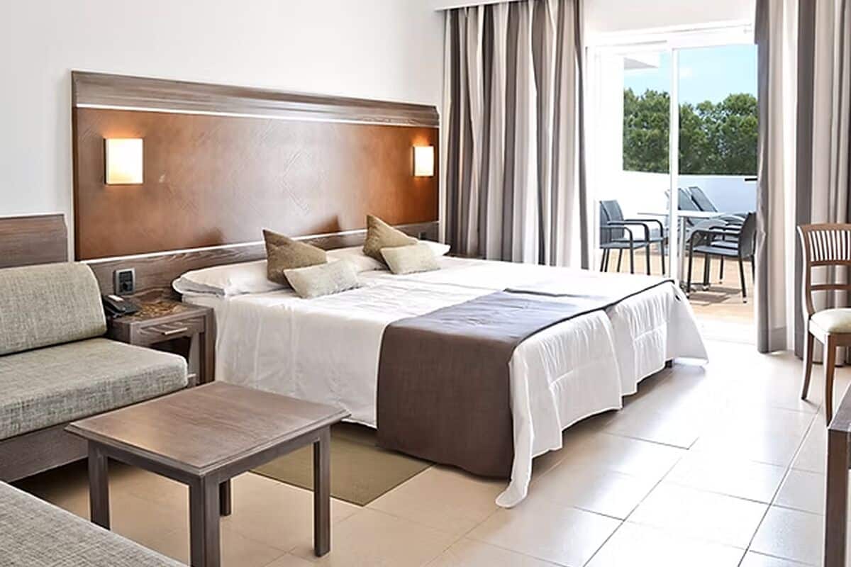 Una habitación de hotel con una cama grande, un sofá, una mesa y un balcón con sillas.