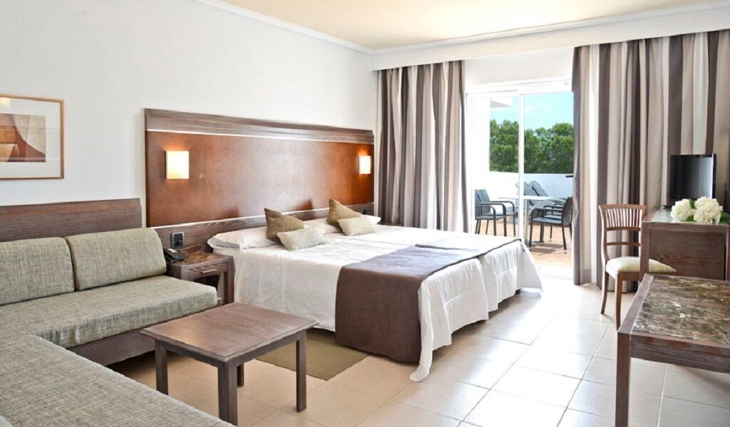 A hotel room with a bed, sofa, and a dining table.