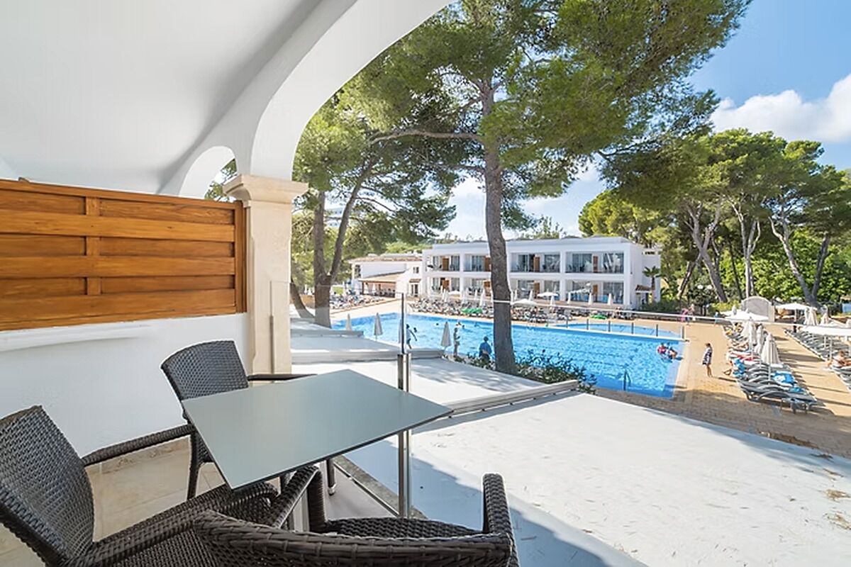 A balcony with wicker furniture overlooking a swimming pool and a white building.