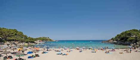 A beach with umbrellas, sun loungers, and people.