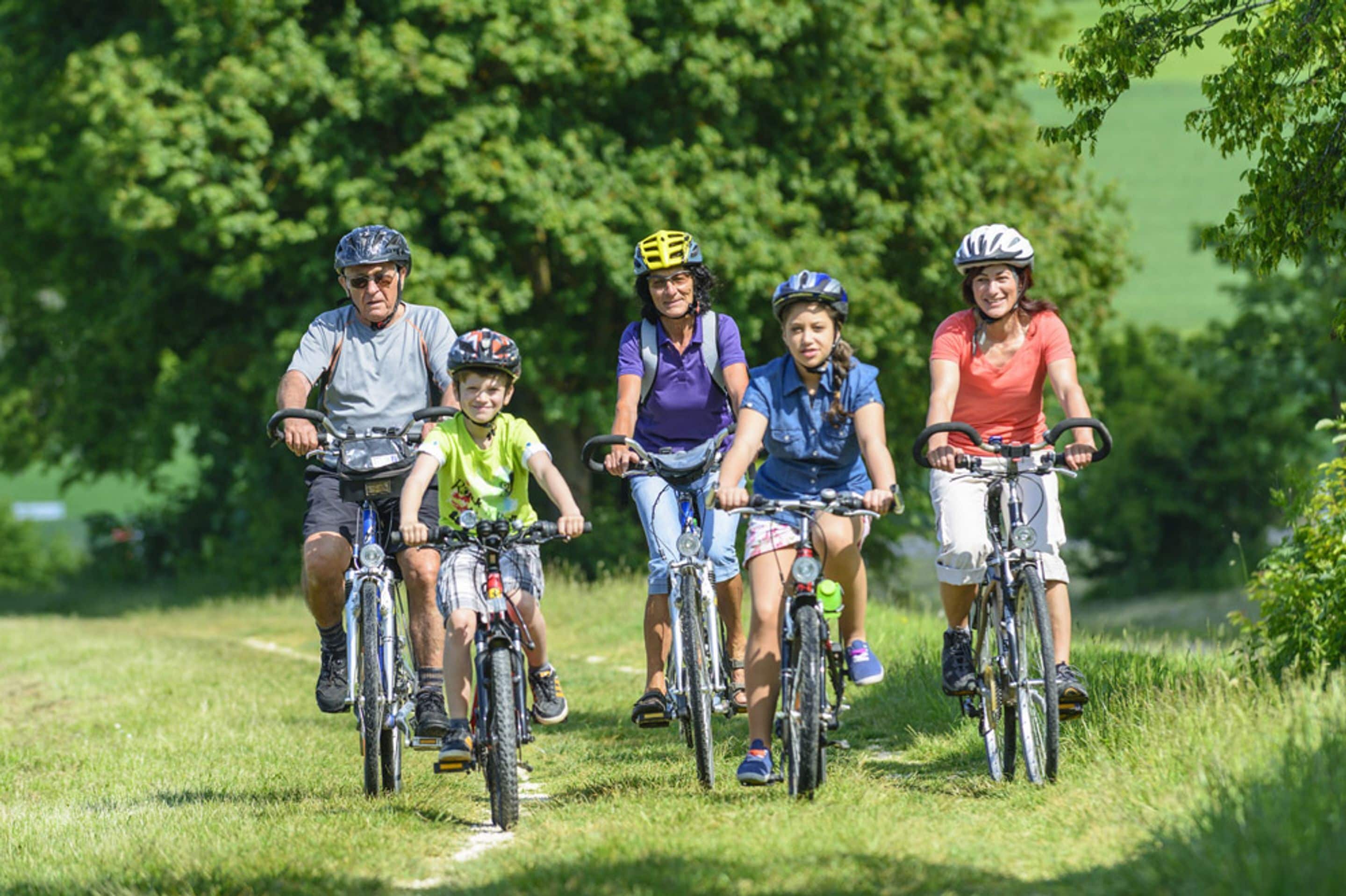 Un grupo de personas en bicicleta sobre un sendero cubierto de hierba, con árboles al fondo.