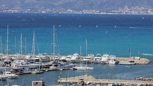 A marina with various boats docked, a rocky breakwater, and a cityscape in the background. - Hotel whala!fun (Llucmajor)