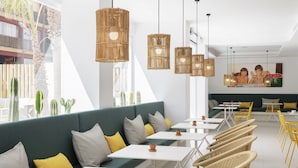 A modern cafe with a green sofa, white tables, wicker chairs, and hanging rattan lights. - Hotel whala!fun (Llucmajor)