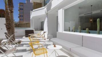 A modern outdoor seating area with yellow chairs, white tables, and a cushioned bench.
