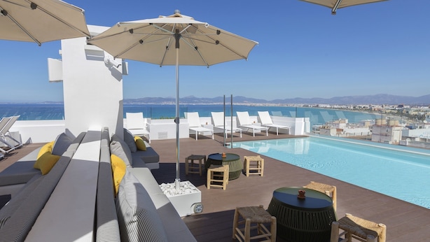 A rooftop pool area with lounge chairs, umbrellas, and a view of the sea. - Hotel whala!fun (Llucmajor)