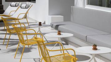 Un espace extérieur moderne, aménagé avec des chaises jaunes et des tables blanches, un canapé gris et un cactus en arrière-plan.