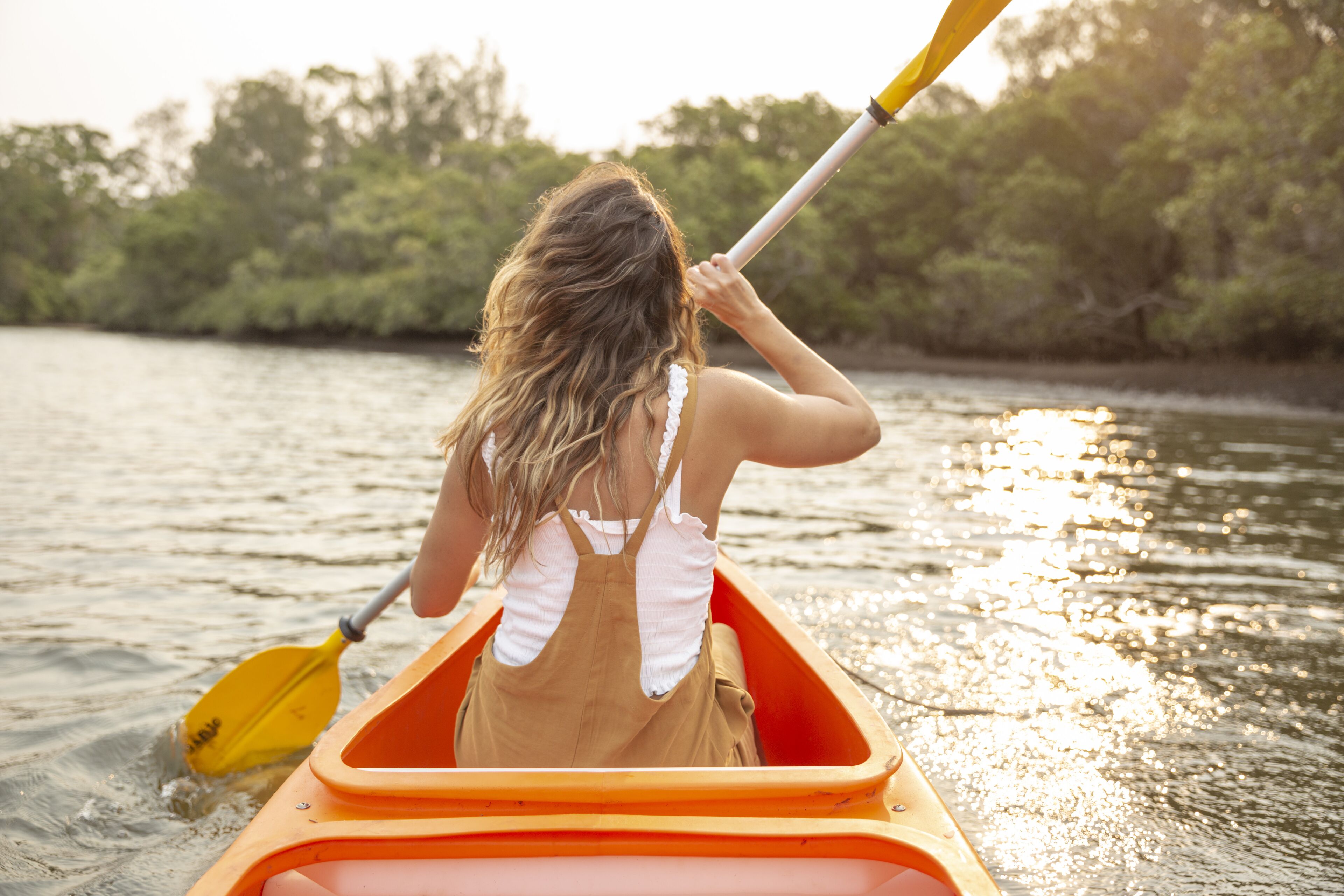 A person in a small orange boat on a body of water with trees in the background.