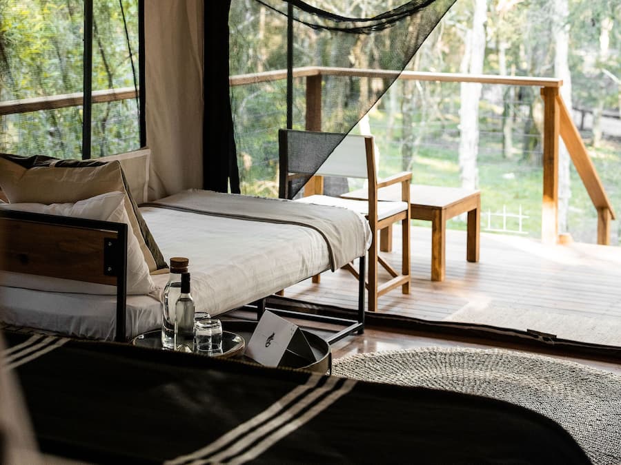A tented accommodation with a bed, a hanging light fixture, and a view of the outdoors.
